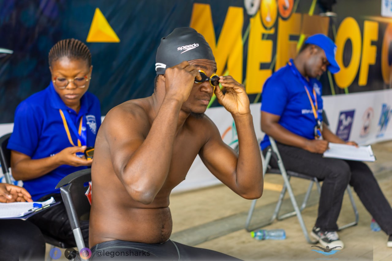 Male swimmer adjusting goggles Meet of Champions banner