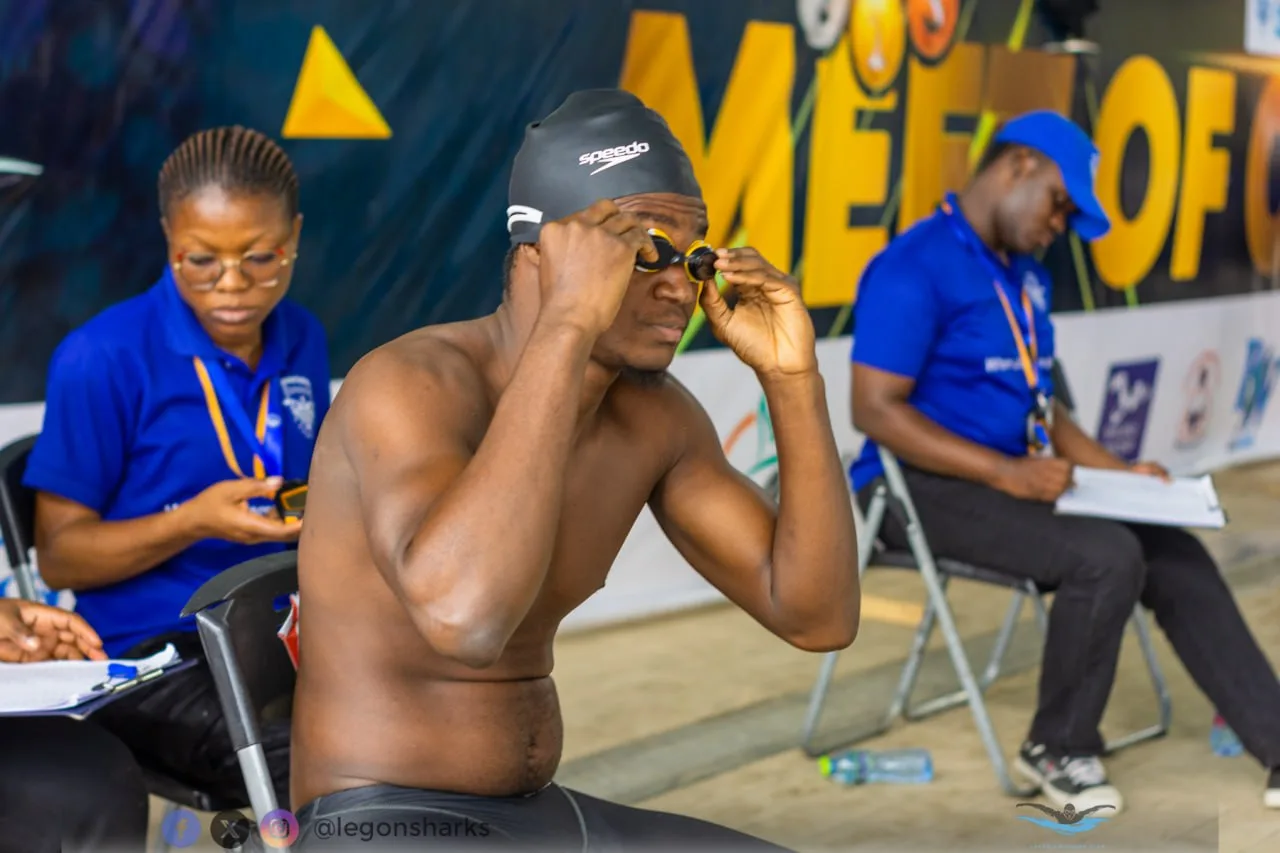 Male swimmer adjusting goggles Meet of Champions banner