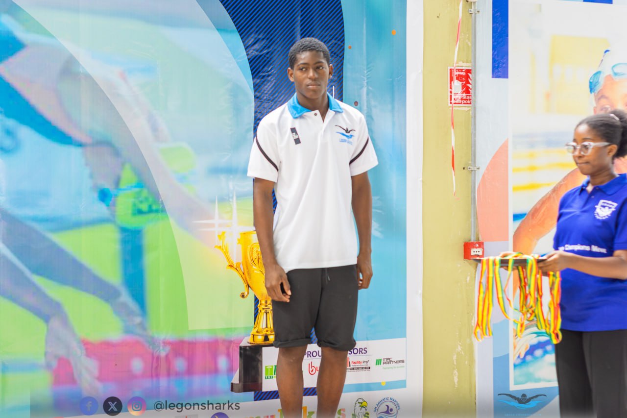 Young male Legon Sharks swimmer on podium with gold trophy